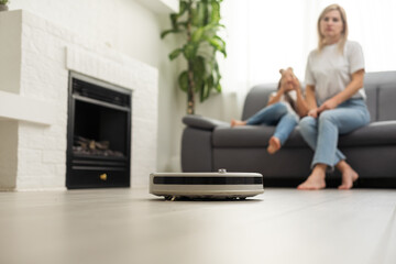 Cute child near mother looking at robotic vacuum cleaner in living room