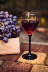 Vertical image of a glass of red wine and partial view of harvested purple grapes in a wooden crate. Viticulture and wine industry. Agricultural hobby and business. Copy ad space