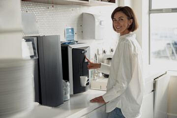 Business woman in casual clothes making a coffee in office kitchen during break. High quality photo