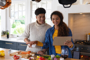 Happy biracial couple preparing food using recipe on tablet in kitchen - Powered by Adobe