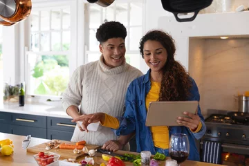 Poster Happy biracial couple preparing food using recipe on tablet in kitchen © wavebreak3