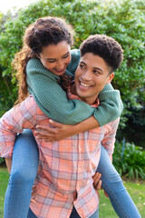 Happy biracial couple having fun piggybacking in garden and smiling