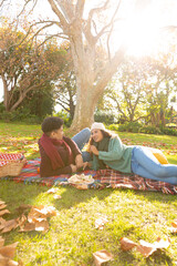 Fototapeta premium Happy biracial couple lying on a rug having picnic and talking in autumn garden