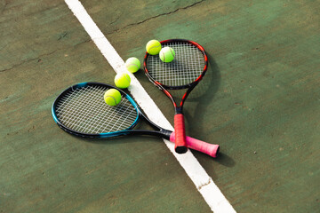 Detail of two tennis rackets and tennis balls lying on the ground at an outdoor tennis court