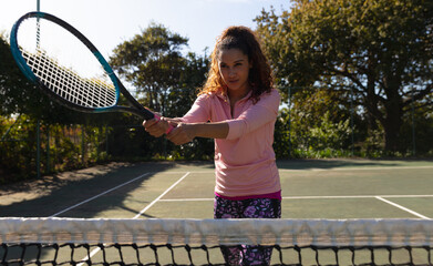 Biracial woman playing tennis swinging racket over the net on sunny outdoor tennis court