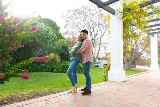 Happy biracial couple embracing and smiling on terrace in garden