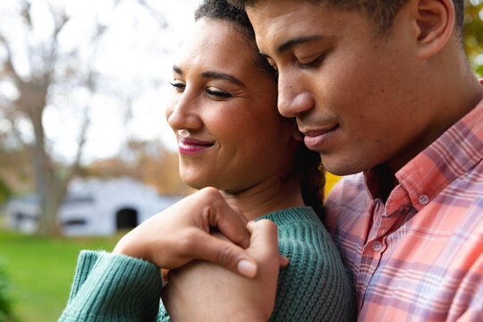 Happy biracial couple embracing and smiling in garden