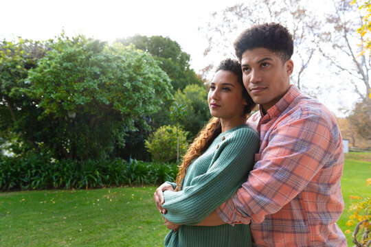 Happy biracial couple embracing and smiling in garden