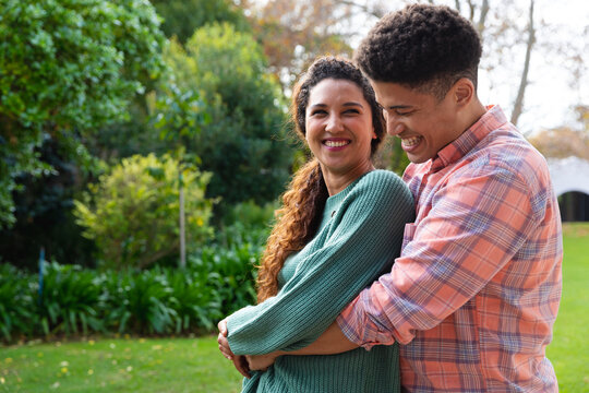 Happy biracial couple embracing and smiling in garden - Powered by Adobe