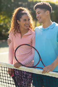 Vertical image of happy diverse couple walking on tennis court and talking
