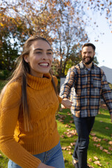 Fototapeta premium Vertical image of happy caucasian couple walking in autumn garden