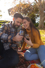 Fototapeta premium Romantic caucasian couple sitting on rug in sunny autumn garden drinking wine