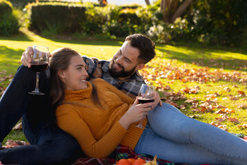 Fototapeta premium Romantic caucasian couple lying on rug in sunny autumn garden drinking wine