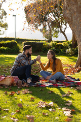 Fototapeta premium Romantic caucasian couple sitting on rug having picnic in sunny autumn garden