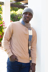 Portrait of happy african american man at home standing in garden wearing hat and scarf