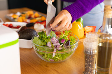 Midsection of caucasian woman standing in kitchen preparing salad