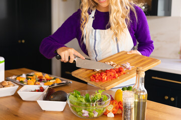 Midsection of smiling caucasian woman standing in kitchen preparing salad