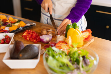 Midsection of caucasian woman standing in kitchen chopping vegetables