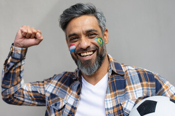 Portrait of happy biracial man with football and flags of netherlands and brazil on cheeks
