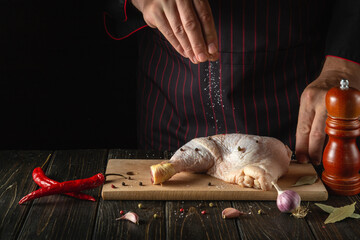 The chef adds salt to the chicken leg in the kitchen. Delicious food recipe concept for hotel or...