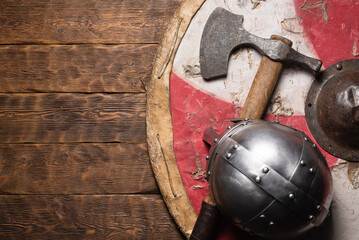 Old battle axe, viking helmet and shield on the wooden table flat lay background with copy space.