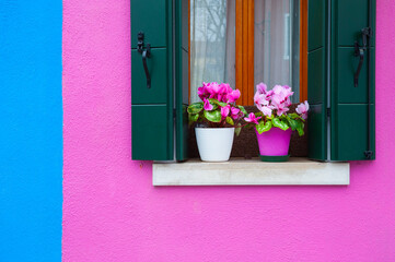Fototapeta na wymiar Pink and blue painted facade of the house and window with pink flowers.