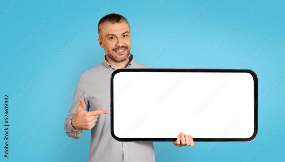 Poster cheerful man holding large smartphone with empty screen, blue background