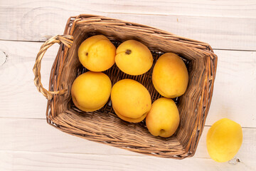 Several bright yellow juicy pineapple apricots in a basket on a wooden table, macro, top view.