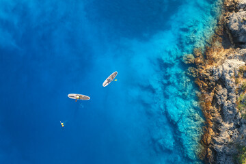 Aerial view of people on floating sup boards on blue sea, rocks, stones at sunset in summer in Oludeniz, Turkey. Tropical landscape. Kayaks on clear water. Active travel. Top view of canoe. Sport