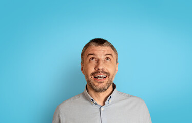 Fototapeta premium Portrait Of Excited Mature Man Looking Up Over Blue Background