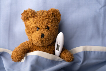 Sick teddy bear on hospital bed with thermometer. Pediatrical and child medicine concept