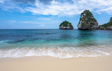 Fototapeta na wymiar Scenery of sunny day with sand beach, turquoise ocean, blue sky, waves and mountains. View of Diamond beach, Nusa Penida, Bali island, Indonesia. Wallpaper background. Natural scenery.