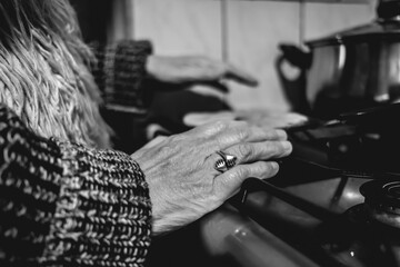 Beautiful hands of elderly latino woman cooking on traditional kitchen stove with gas burners with traditional toaster with 'sopaipillas' (fried pastry) and pots (in black and white)
