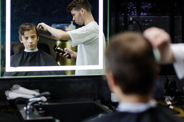 Young male barber cutting teenage boy's hair in barbershop.