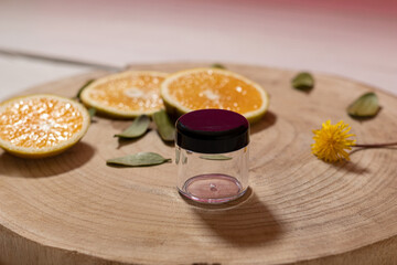 Frasco de vidrio transprente, con tapa negra, sin marca con hojas verdes y rebanadas de naranja sobre tabla de madera