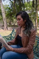 portrait of a beautiful latina woman sitting on a bench in the park reading book