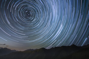 silhouetted mountains with circumpolar star trails in northern sky - obrazy, fototapety, plakaty