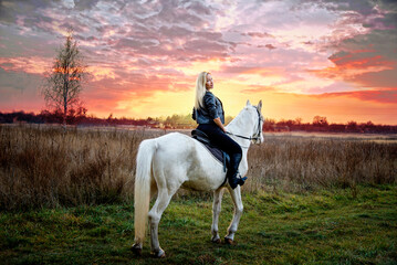 young beautiful blond smiling woman with long hair  riding a white horse with blue eyes in autumn...