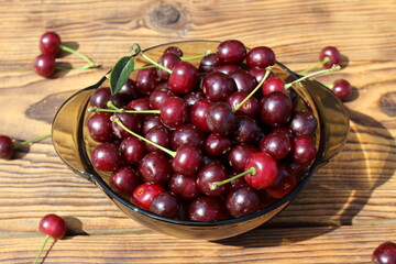 A bowl with many cherries stands on a wooden background.