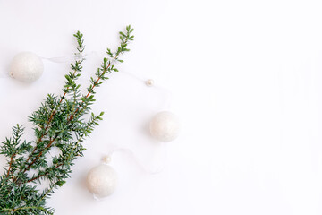 Fototapeta na wymiar White garland. New Year's decoration and a twig of a Christmas tree or juniper on a white background. Round balls with a ribbon. Flat lay. Copy space for text, greeting card. Soft selective focus.