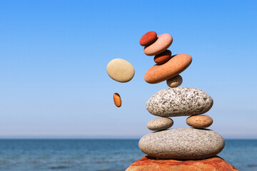 The fall of the pyramid of balanced stones on blue sky background. The concept of fall risk and...