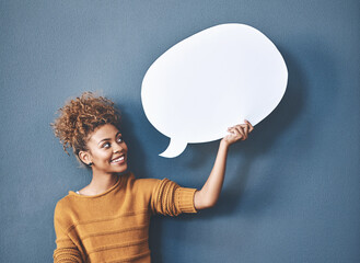 Young woman holding a speech bubble against a grey background in a studio. Portrait of a casual, happy and smiling female holding copy space empty shape for social media, chat and voice or message. - obrazy, fototapety, plakaty