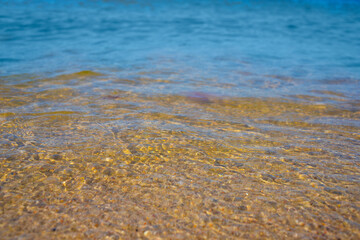Close-up of the sea coast, clear sea water with shallow waves and a narrow washes the shore with a smooth brown sandy surface.
