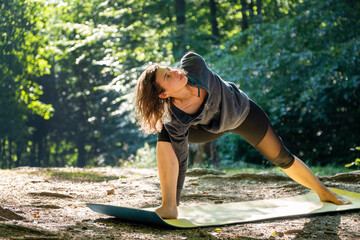 Morning view of pretty young woman performing yoga asanas on a meadow in the forest. Travel and healthy lifestyle, enjoying nature