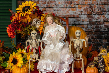 Halloween still life with doll surrounded by skeletons pumpkins and sunflowers
