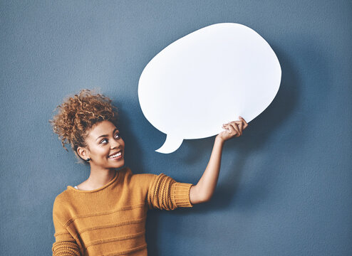 Young woman holding a speech bubble against a grey background in a studio. Portrait of a casual, happy and smiling female holding copy space empty shape for social media, chat and voice or message.