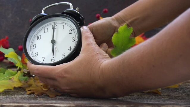 Autumn time - someones hands changing time, one hour back on alarm clock, slow motion