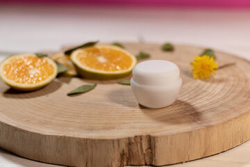 Frasco de crema blanco, sin marca con hojas verdes y rebanadas de naranja sobre tabla de madera
