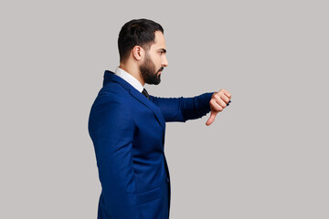 Side view of bearded man criticizing bad quality with thumbs down displeased grimace, showing...