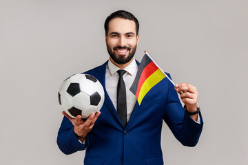 Positive bearded man holding flag of germany and soccer black and white classic ball and watching...
